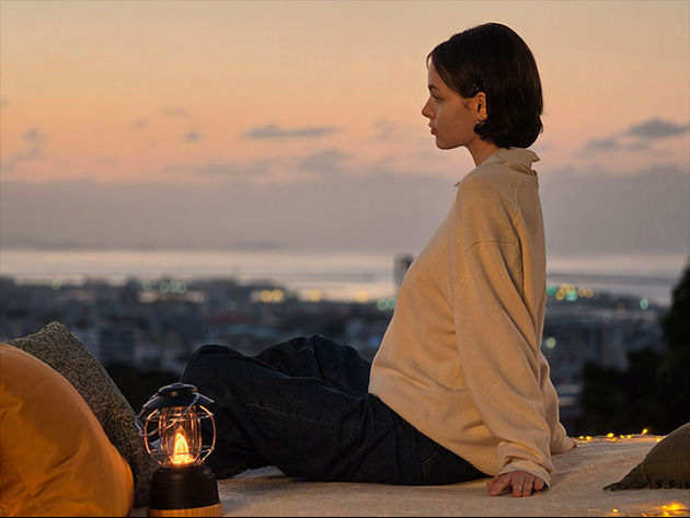 Photo taken with the Samsung Galaxy S26 Ultra main camera in low light. A side-profile, low-light portrait of a person sitting on a rooftop at dusk, looking out over a blurred city skyline.