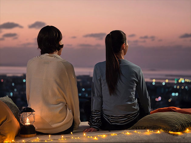 Photo taken with the Samsung Galaxy S26 Ultra main camera in low light. Two people sit side-by-side on a rooftop overlooking a city at dusk.