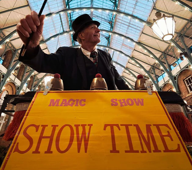 A low angle wide angle shot taken with the Xiaomi 15 Ultra featuring a magician in a top hat holding a wand behind a bright yellow Magic Show sign A low-angle wide-angle shot taken with the Xiaomi 15 Ultra featuring a magician in a top hat holding a wand behind a bright yellow 'Magic Show' sign.