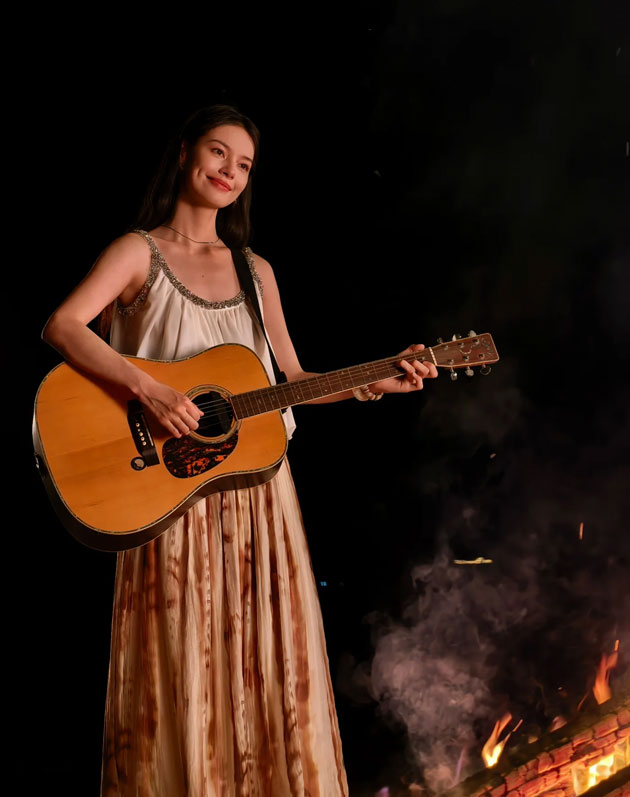 A low light night photograph taken with the Huawei Pura 80 Ultra featuring a woman playing an acoustic guitar next to a campfire A low-light night photograph taken with the Huawei Pura 80 Ultra, featuring a woman playing an acoustic guitar next to a campfire.
