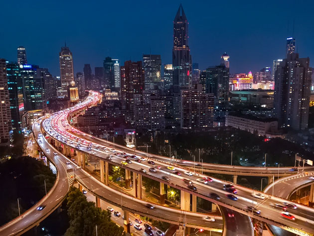 A night-time cityscape camera sample from the Realme C71, showing a winding multi-level highway with flowing traffic lights against a backdrop of illuminated skyscrapers and a dark blue sky.