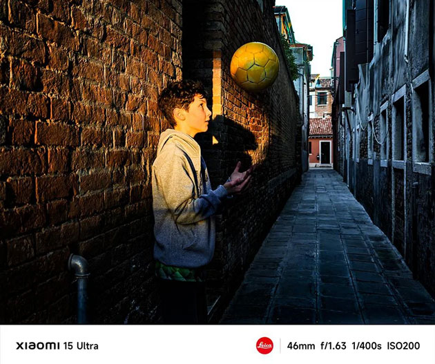 A sharp action shot captured on the Xiaomi 15 Ultra at a 46mm focal length A sharp action shot captured on the Xiaomi 15 Ultra at a 46mm focal length, featuring a boy tossing a yellow soccer ball into the air within a narrow, shadowed alley.