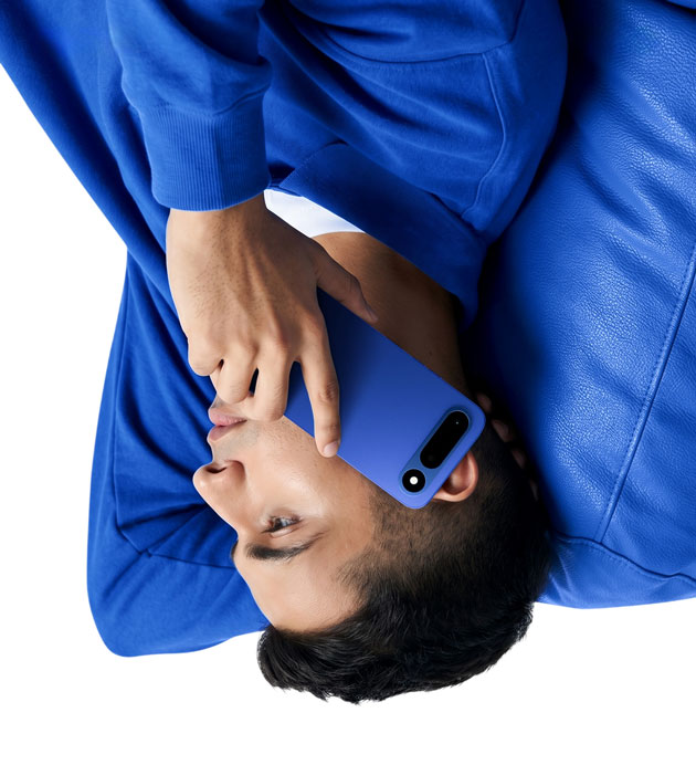 A side profile upside down lifestyle shot of a person lying on a blue leather surface holding the Tecno Pop X Midnight Blue smartphone to their ear A side-profile, upside-down lifestyle shot of a person lying on a blue leather surface, holding the Tecno Pop X Midnight Blue smartphone to their ear.