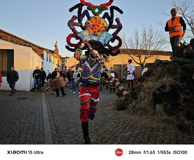 A vibrant action shot captured on the Xiaomi 15 Ultra at 28mm A vibrant action shot captured on the Xiaomi 15 Ultra at 28mm, featuring a festival performer in an elaborate, colorful costume and mask dancing down a cobblestone street.