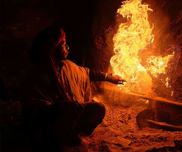 Cinematic low light shot of a man by a fire demonstrating the Xiaomi 15 Ultras dynamic range and color reproduction A low-light, high-contrast photograph captured on the Xiaomi 15 Ultra showing a man in a red turban crouched beside a large, vibrant fire.