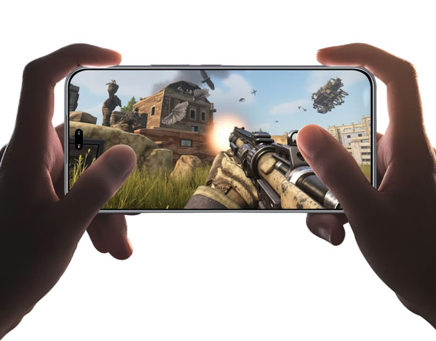 Hands holding a Honor 400 Pro in landscape mode displaying a first person shooter game with a gun and battlefield scene Hands holding a Honor 400 Pro in landscape mode, displaying a first-person shooter game with a gun and battlefield scene.