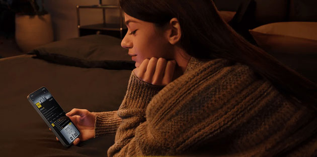 A young woman lies comfortably in a dimly lit bedroom holding the Poco X8 Pro Max to browse content in low light conditions A young woman lies comfortably in a dimly lit bedroom, holding the Poco X8 Pro Max to browse content in low-light conditions.