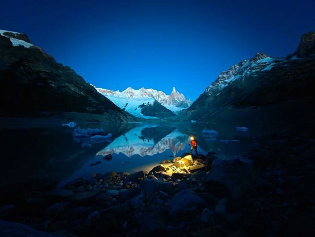 Night photo of a valley and snowy mountains with a clear reflection in calm water and a single light in the foreground; captured with OPPO Find X9 Ultra camera