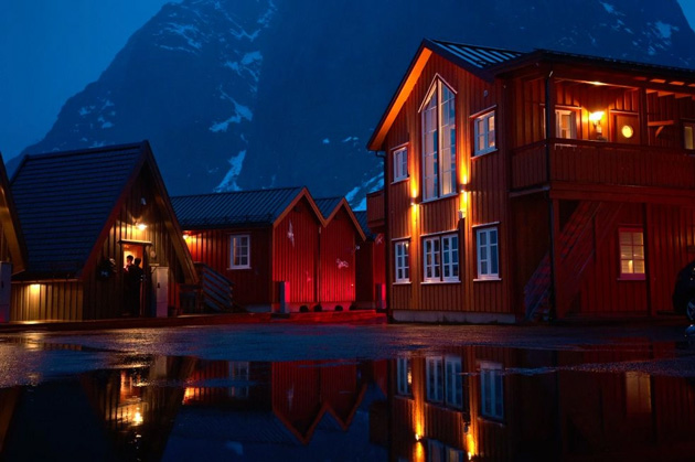 Night view of red wooden houses with warm lights and reflection on still water, among snowy mountains; calm and cinematic atmosphere; photo taken with OPPO Find X9 Ultra camera