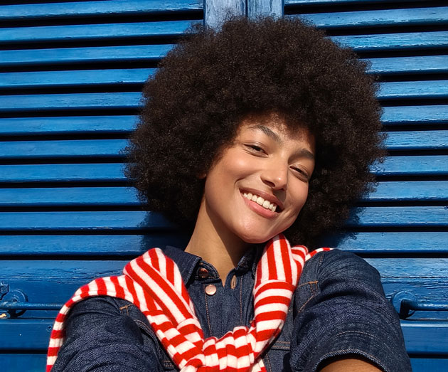 A selfie taken with the Xiaomi Redmi Note 15 Pro 5G showing a curly haired woman in front of blue wooden shutters under bright sunlight A selfie taken with the Xiaomi Redmi Note 15 Pro 5G showing a curly-haired woman in front of blue wooden shutters under bright sunlight.